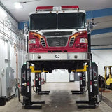 Fire truck elevated on a vehicle lift in a maintenance garage.