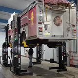 Pink fire truck elevated on hydraulic lifts in a maintenance bay.