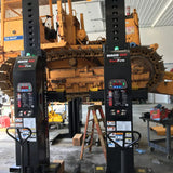 Heavy construction equipment, likely a bulldozer or excavator, suspended between two lift columns for maintenance or repair.