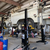 Utility truck elevated on hydraulic lifts in a repair garage.