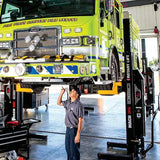 Bright green fire engine lifted on a hydraulic lift in a maintenance bay.