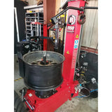 Tire changing machine with a red frame and a black wheel mounted on it.