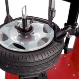 Tire mounted on a wheel balancing machine with a red base.